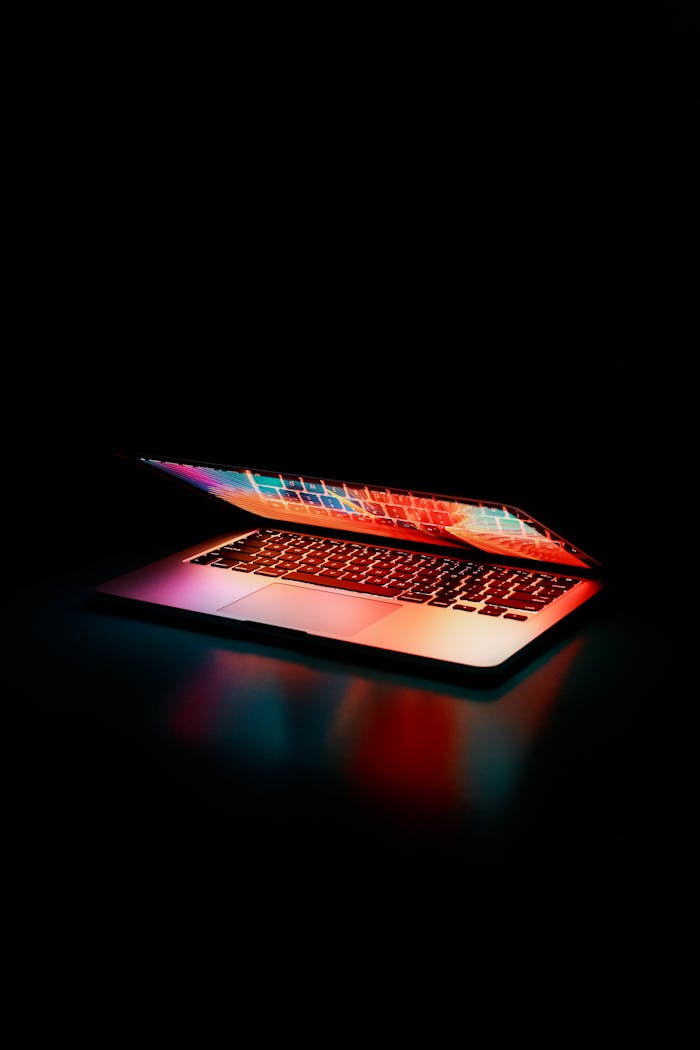 our-services-1 Laptop partially opened, emitting vibrant multicolored lights in dark setting.