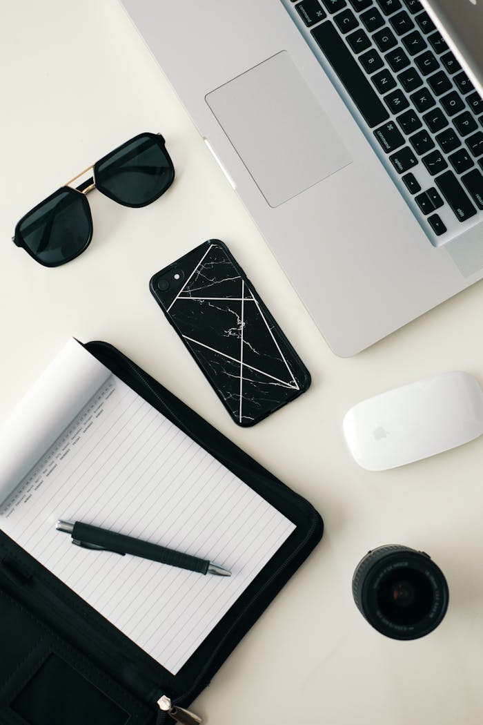 our-services-3 A clean workspace featuring a laptop, smartphone, sunglasses, and stationery on a white surface.
