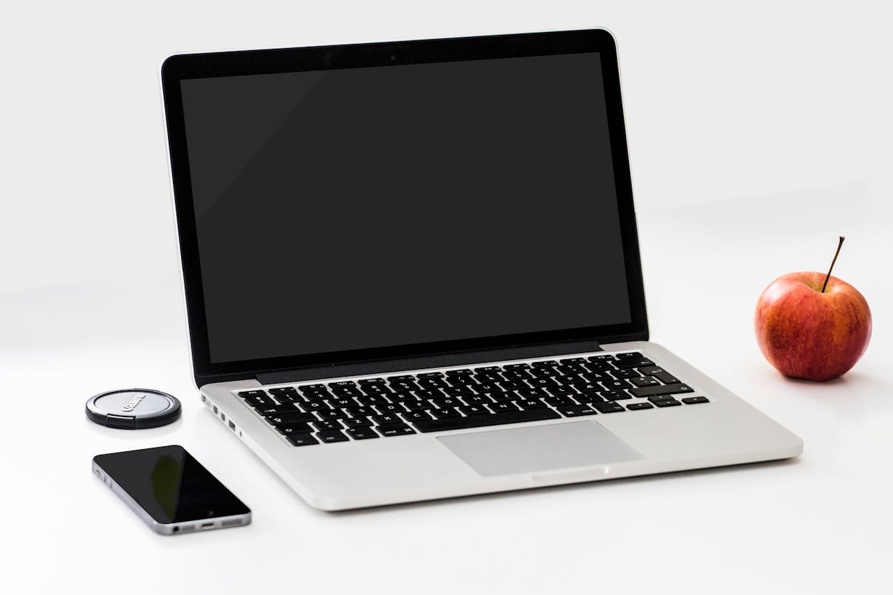 ours-journey A minimalist workspace featuring a laptop, smartphone, and an apple on a clean white desk.